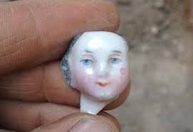 Picture of the head of a frozen charlotte doll found at the dig sight being held in a hand.